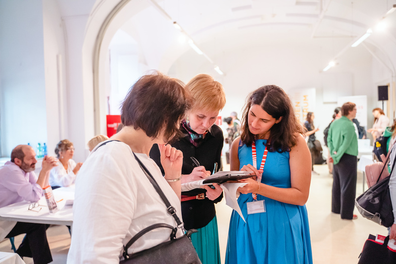 Drei Frauen diskutieren und notieren Informationen in einem geschäftigen Veranstaltungsraum.