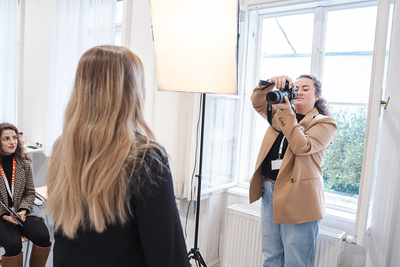 Eine Frau posiert für ein Fotoshooting, während eine andere Frau mit einer Kamera fotografiert.