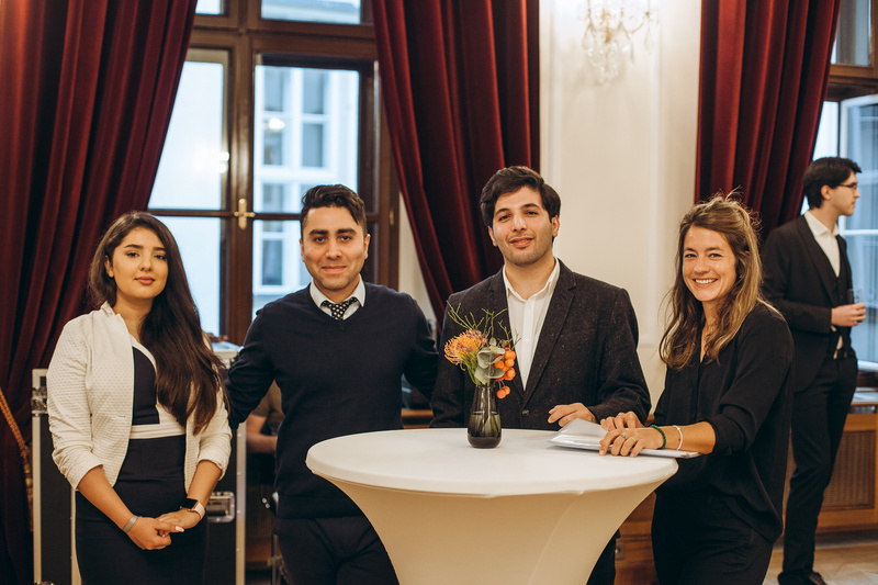 Vier Personen stehen an einem Stehtisch mit einer Blumenvase in einem elegant eingerichteten Raum.