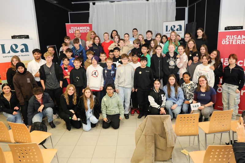 Gruppenfoto von Jugendlichen und Erwachsenen bei einer Veranstaltung, im Hintergrund Banner mit den Texten „Zusammen: Österreich“ und „Lea“.