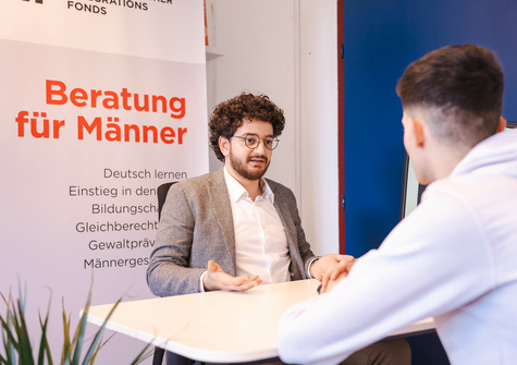 Beratungsgespräch zwischen zwei Männern über Unterstützung für Männer in verschiedenen Lebensbereichen.