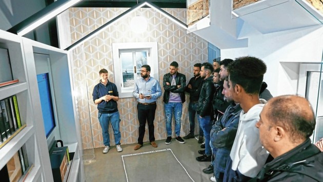 Eine Gruppe von Menschen hört einem Vortrag in einem modernen, hausähnlichen Raum zu.