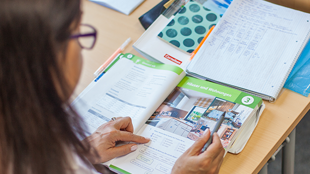 Eine Person liest in einem Lehrbuch über Wohnungen und zeigt auf eine Abbildung.