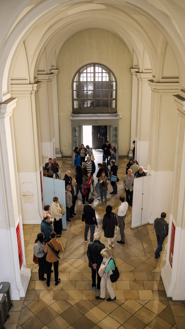 Menschen stehen in einem weitläufigen Raum mit hohen Decken und genießen eine Veranstaltung oder Ausstellung.