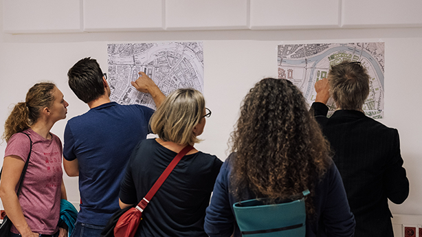 Eine Gruppe von Menschen betrachtet Pläne an der Wand und zeigt mit dem Finger darauf.