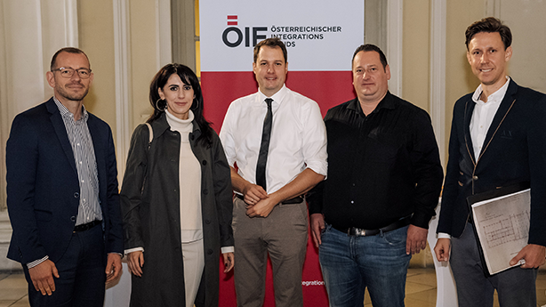 Fünf Personen stehen vor einem Banner des Österreichischen Integrationsfonds und posieren für ein Foto.