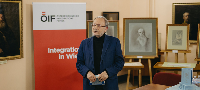 Ein Mann steht vor einem roten Banner des Österreichischen Integrationsfonds und spricht über Integration in Wien.